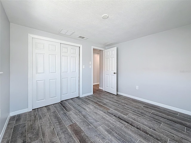 unfurnished bedroom featuring a textured ceiling, baseboards, dark wood-type flooring, visible vents, and a closet