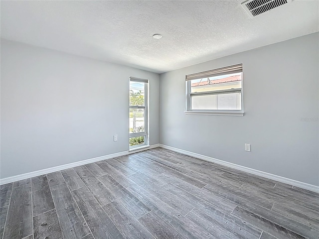 empty room with baseboards, dark wood finished floors, a textured ceiling, and visible vents