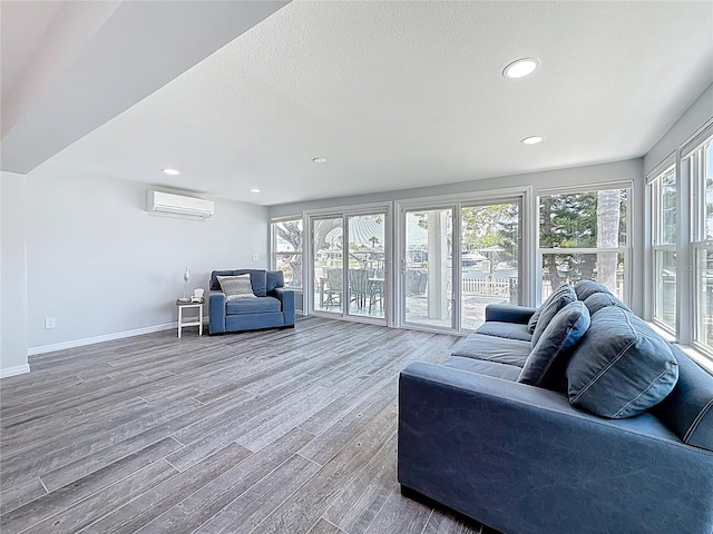 living room featuring wood finished floors, baseboards, plenty of natural light, and a wall mounted AC