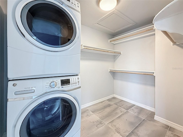 clothes washing area with stacked washing maching and dryer, baseboards, laundry area, and attic access