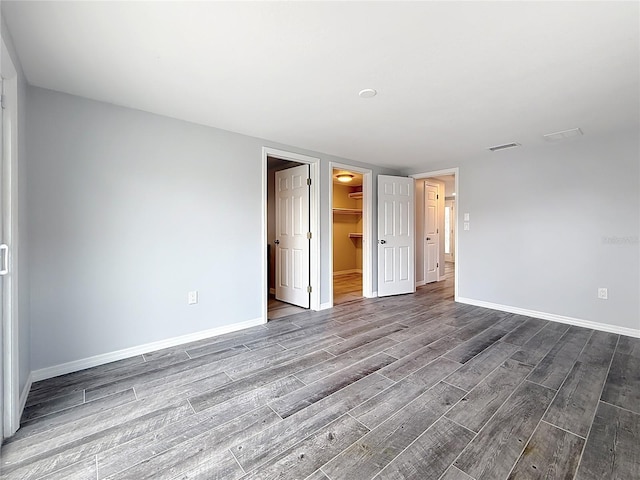 unfurnished bedroom with baseboards, visible vents, wood finished floors, and a spacious closet