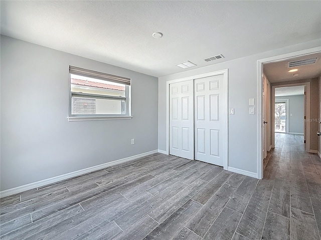 unfurnished bedroom featuring baseboards, multiple windows, wood finished floors, and visible vents