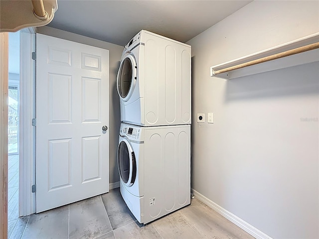 washroom featuring stacked washer / drying machine, baseboards, and laundry area
