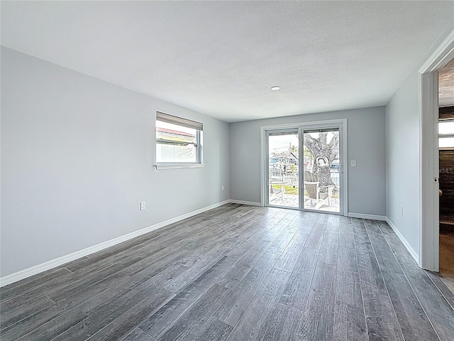unfurnished living room featuring dark wood-style flooring, baseboards, and a wealth of natural light