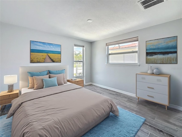 bedroom with visible vents, a textured ceiling, baseboards, and wood finished floors