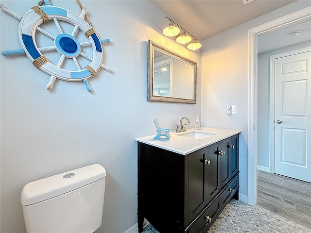 half bathroom featuring toilet, baseboards, wood finished floors, and vanity