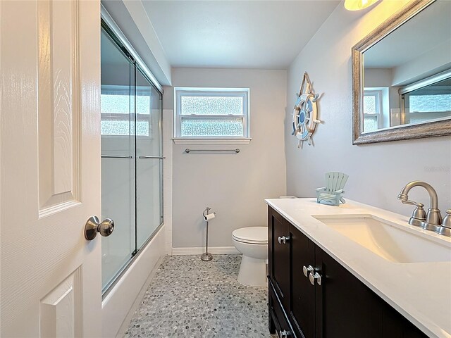 full bathroom featuring vanity, toilet, speckled floor, baseboards, and bath / shower combo with glass door