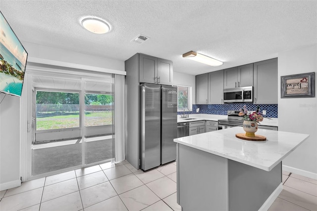 kitchen with light stone counters, a sink, gray cabinets, stainless steel appliances, and decorative backsplash
