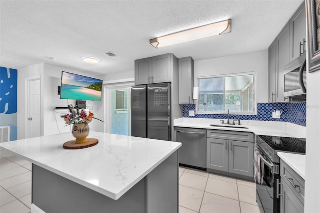 kitchen with a sink, a textured ceiling, gray cabinets, stainless steel appliances, and visible vents