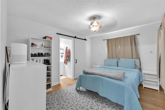 bedroom with a barn door, a textured ceiling, and wood finished floors