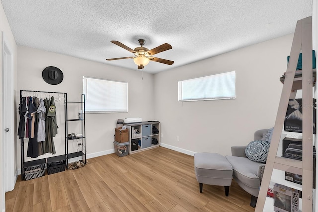 sitting room featuring a ceiling fan, baseboards, a textured ceiling, and light wood-style floors