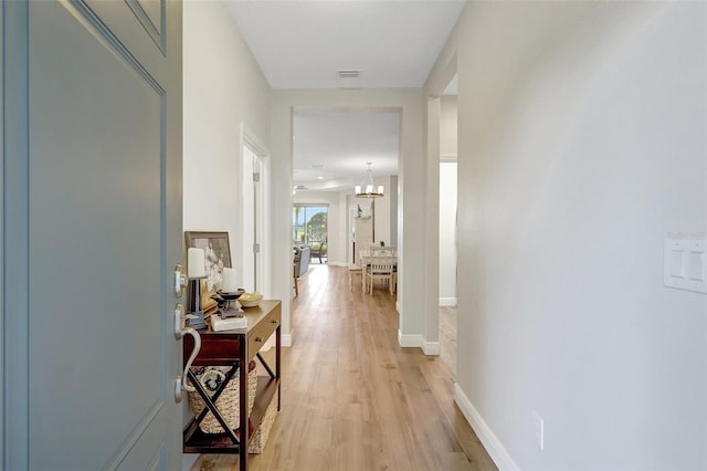 hall featuring baseboards, light wood finished floors, and visible vents
