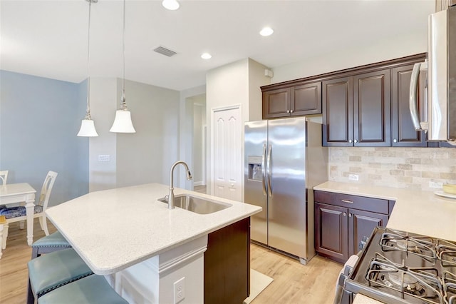 kitchen with appliances with stainless steel finishes, a sink, light wood-style flooring, backsplash, and visible vents
