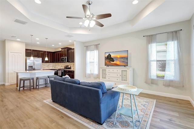 living area featuring baseboards, a tray ceiling, and light wood-type flooring