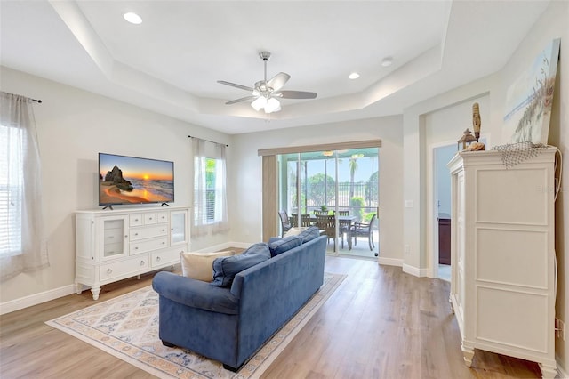living room with baseboards, a tray ceiling, ceiling fan, and light wood-type flooring