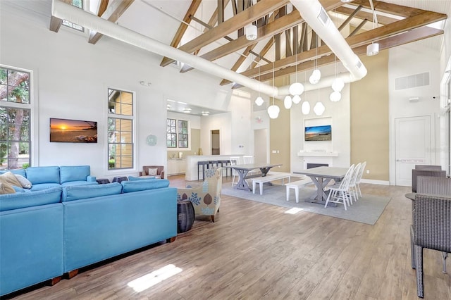 living room featuring high vaulted ceiling, beamed ceiling, light wood-type flooring, and visible vents
