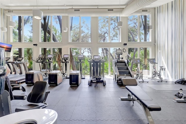 exercise room featuring visible vents, a towering ceiling, and a healthy amount of sunlight