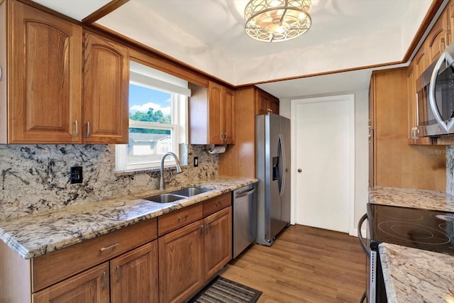 kitchen featuring brown cabinetry, a sink, light wood finished floors, and appliances with stainless steel finishes