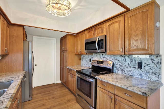 kitchen with light stone counters, decorative backsplash, appliances with stainless steel finishes, and light wood-type flooring