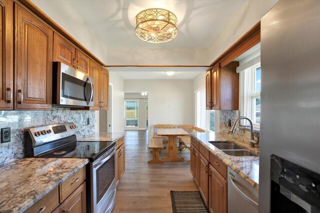 kitchen with wood finished floors, light stone countertops, tasteful backsplash, a sink, and appliances with stainless steel finishes