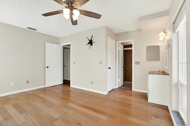 unfurnished bedroom featuring ceiling fan, visible vents, a sink, baseboards, and light wood-style floors