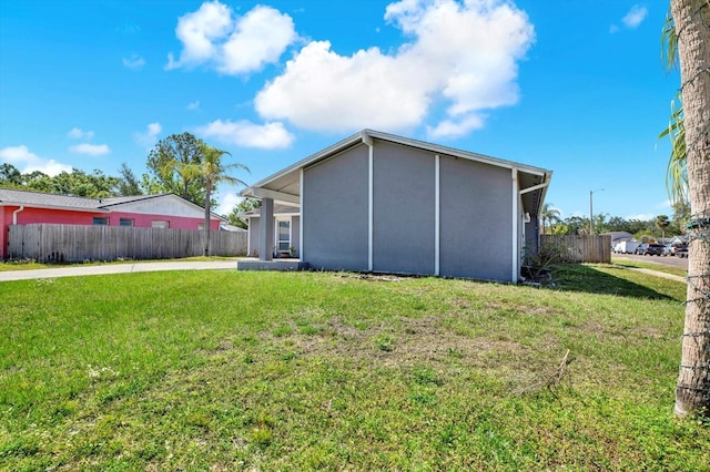 rear view of house featuring fence, stucco siding, a lawn, and driveway