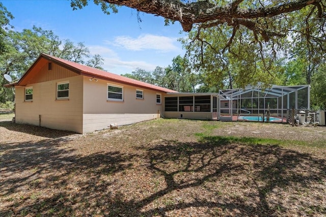 rear view of property with a sunroom, a lanai, an outdoor pool, and concrete block siding