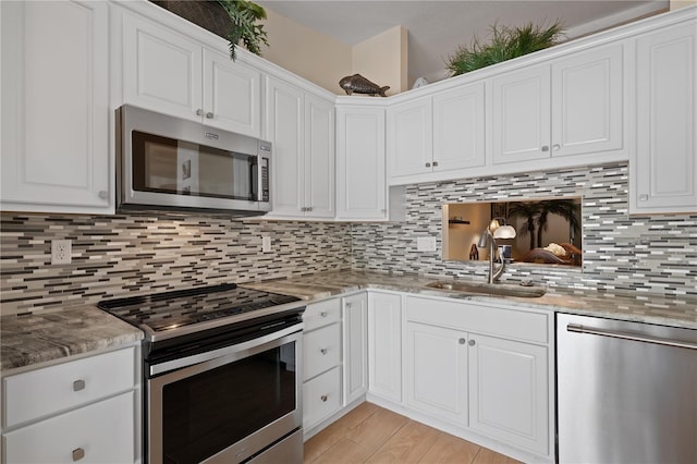 kitchen with stainless steel appliances, white cabinetry, a sink, and tasteful backsplash