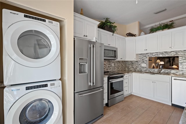 kitchen featuring decorative backsplash, visible vents, stacked washing maching and dryer, white cabinets, and stainless steel appliances