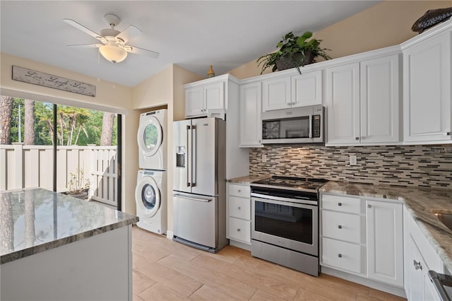 kitchen with stacked washer / drying machine, ceiling fan, white cabinets, appliances with stainless steel finishes, and backsplash