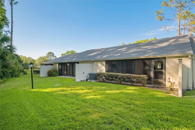 back of property featuring central AC, a shingled roof, stucco siding, and a yard