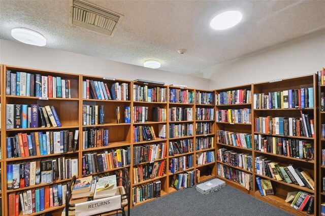 sitting room featuring carpet flooring, a textured ceiling, wall of books, and visible vents