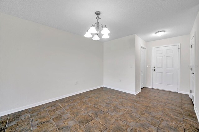 unfurnished room featuring baseboards, a textured ceiling, stone finish flooring, and a chandelier