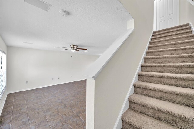 stairway with baseboards, a ceiling fan, a textured ceiling, and visible vents