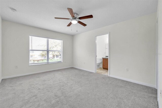 unfurnished bedroom with baseboards, light carpet, a ceiling fan, and ensuite bath