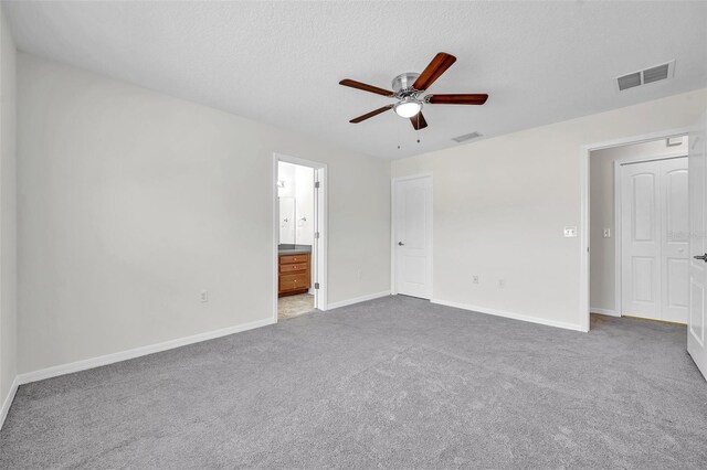 unfurnished bedroom featuring visible vents, baseboards, ensuite bathroom, a textured ceiling, and carpet flooring