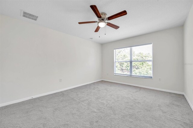 empty room with carpet floors, ceiling fan, visible vents, and baseboards