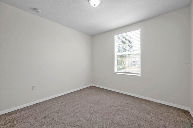 carpeted empty room featuring a textured ceiling and baseboards