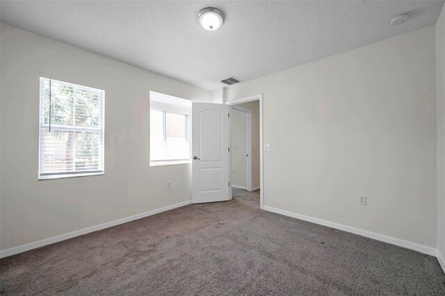 carpeted spare room featuring visible vents, a textured ceiling, and baseboards