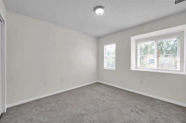 carpeted spare room featuring baseboards, a textured ceiling, and visible vents