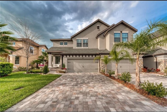 traditional-style home with an attached garage, decorative driveway, stucco siding, and a front yard