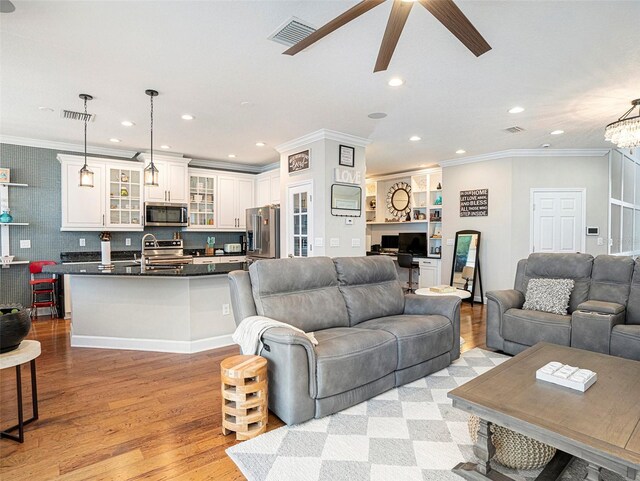living area with light wood-style floors, ornamental molding, ceiling fan with notable chandelier, and visible vents