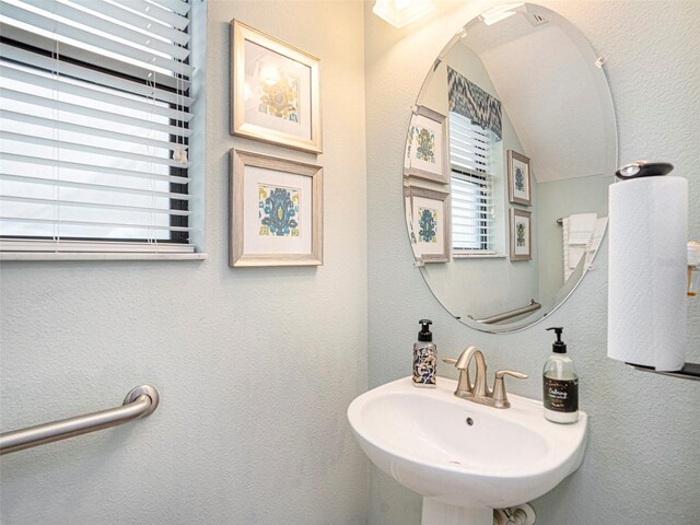 bathroom featuring a sink, a textured wall, and lofted ceiling