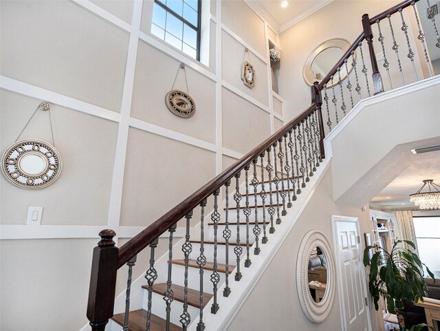 staircase featuring ornamental molding, a towering ceiling, and a notable chandelier
