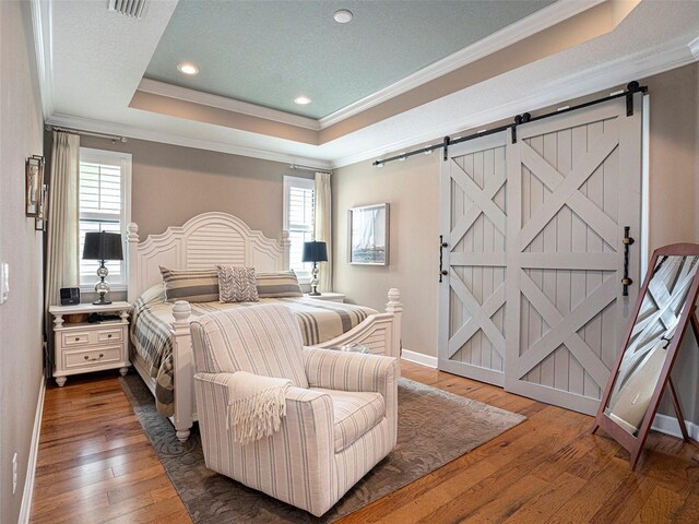 bedroom featuring a tray ceiling, a barn door, ornamental molding, and multiple windows
