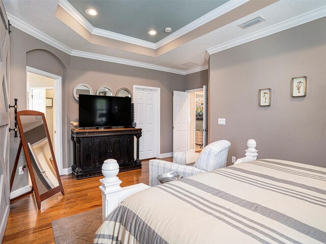 bedroom with visible vents, arched walkways, light wood-type flooring, baseboards, and a tray ceiling