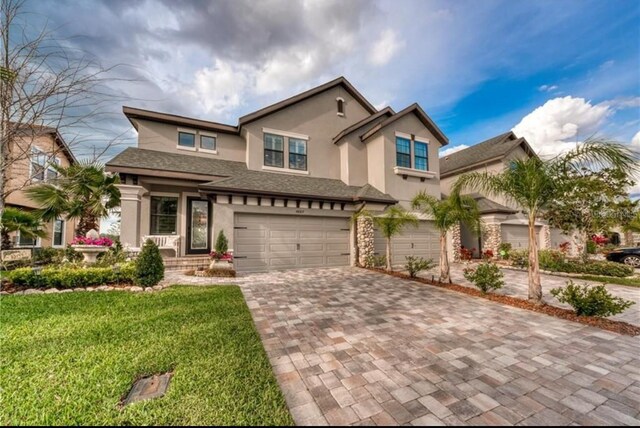 view of front facade with an attached garage, stucco siding, a front lawn, and decorative driveway