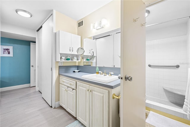 full bath featuring vanity, visible vents, wood finished floors, baseboards, and tiled shower