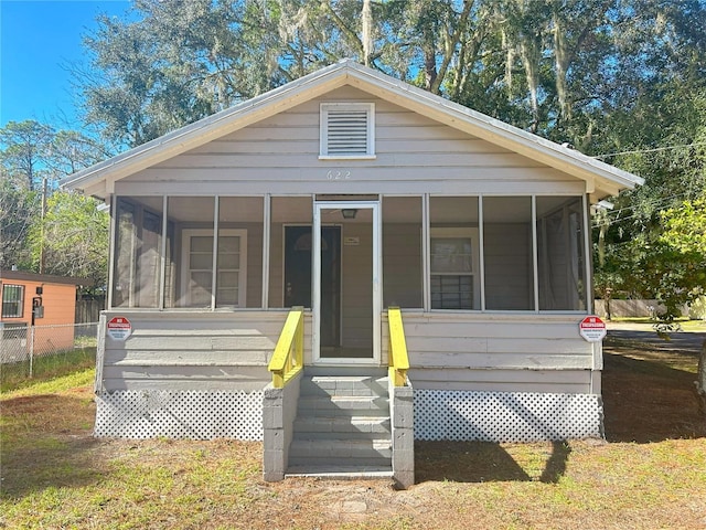 rear view of house with fence, entry steps, and a sunroom