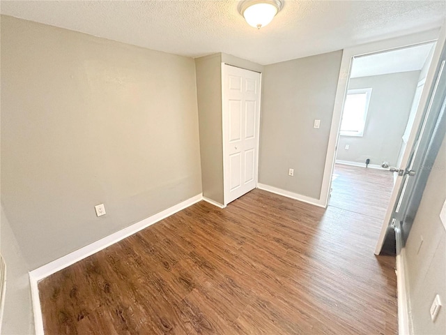 unfurnished bedroom featuring a textured ceiling, baseboards, a closet, and wood finished floors